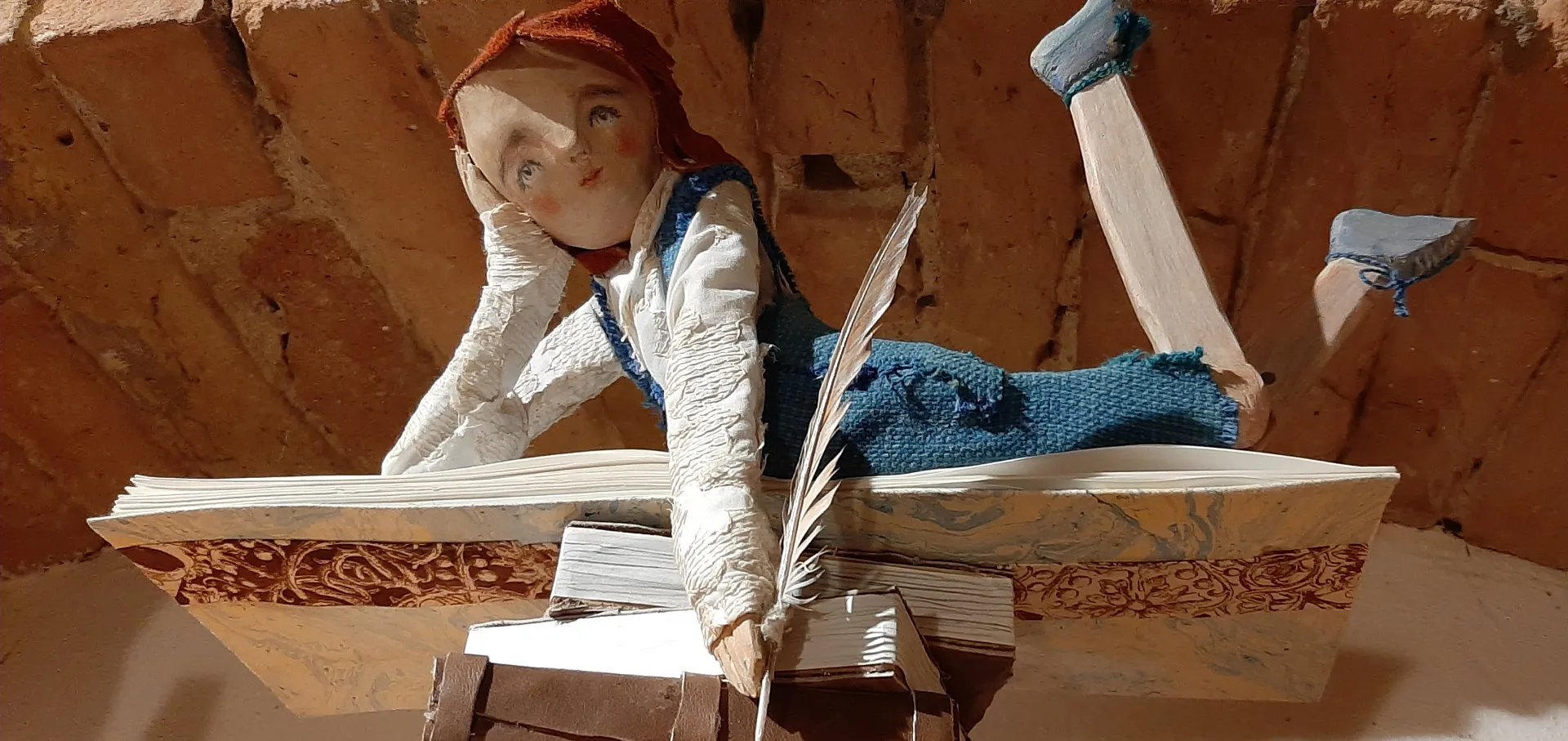 Una bambola di stoffa e legno, sdraiata su un grande libro, scrive con una piuma.